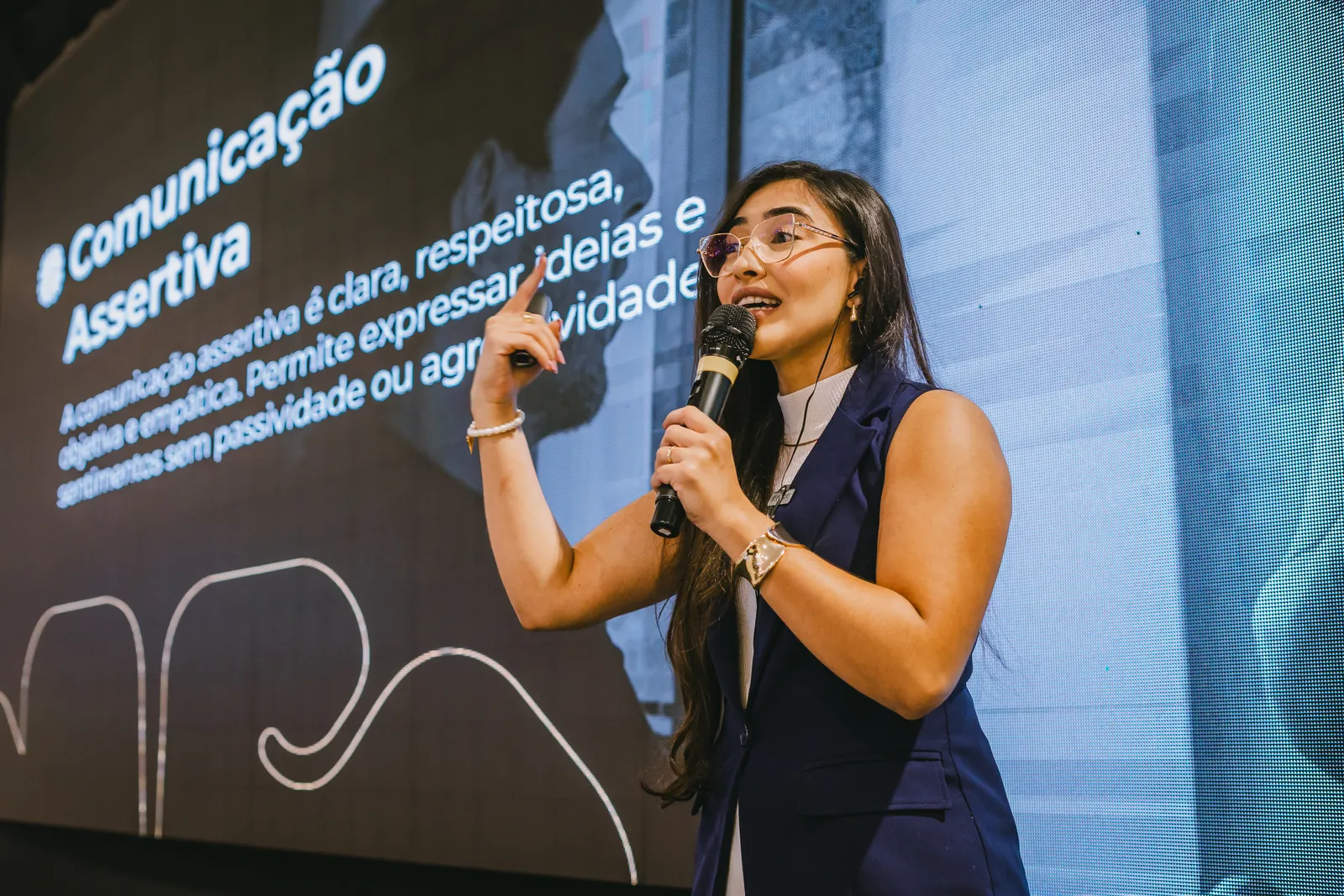 Ynnara palestrando sobre Comunicação Assertiva, com o microfone na mão