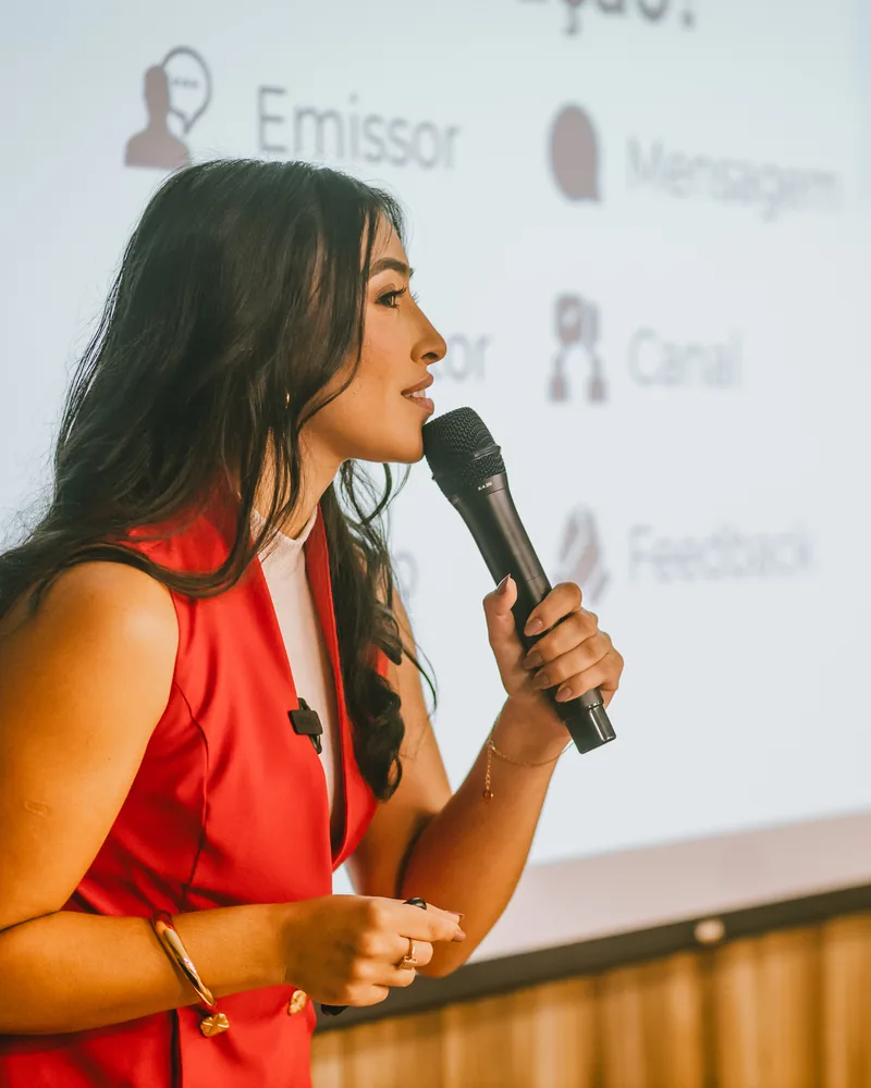 Ynnara falando ao microfone diante de um slide sobre comunicação